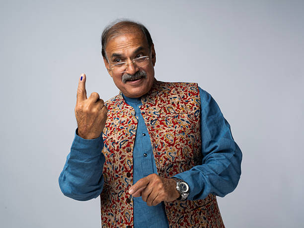 Portrait of smiling senior man in traditional attire showing index finger with voting ink sign while standing over white background