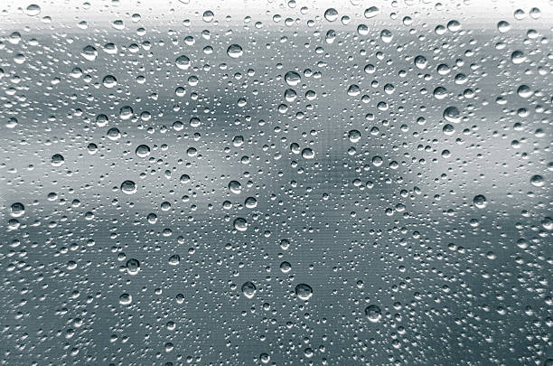 Raindrops clinging to a windowpane, creating a textured surface against a blurred background of overcast weather