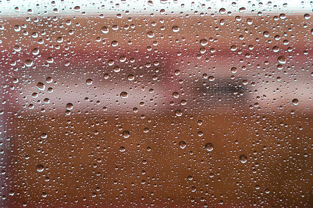 Raindrops covering a glass window, creating a natural wet texture with an abstract brown and red blurred background