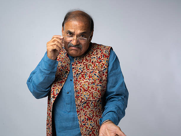 Portrait of sad, serious retired Indian senior men sitting on the chair in a room and contemplating deeply by hand on chin with blank expression at home.