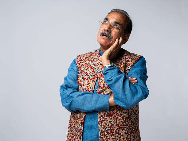 Portrait of thoughtful senior male politician dressed in kurta posing with hand on chin against white background