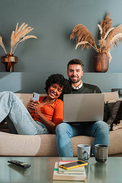 istock Happy couple enjoying technology together while using smartphone and laptop in their cozy living room 2250985351