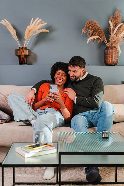 istock Happy couple sharing joyful moments while using a smartphone together on a cozy couch at home 2250986388