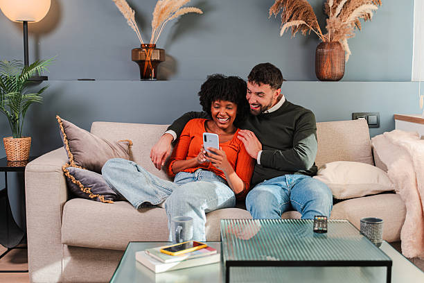 istock Joyful couple enjoying quality time together while using a smartphone on a cozy couch in their home 2250988161