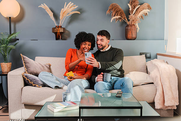 Joyful couple sharing a delightful moment together while using their smartphone on a comfortable couch