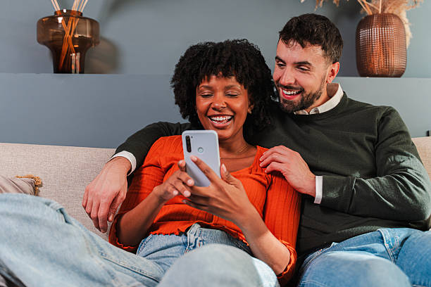 istock Joyful couple sharing moments together while using a smartphone on a cozy couch at home 2250989454