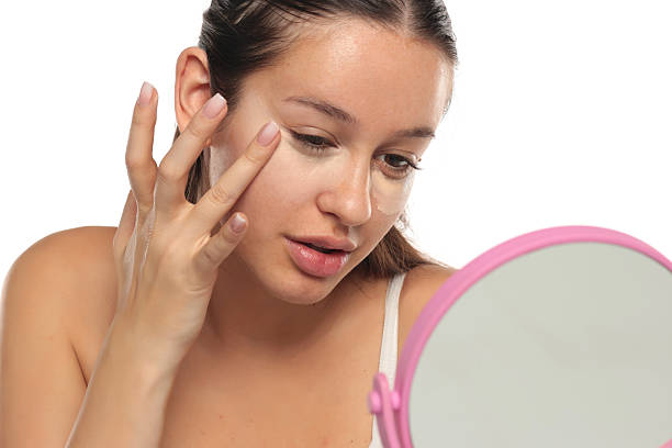 istock Young woman blending concealer under her eyes while looking in a mirror, studio shot on a white background 2250990804
