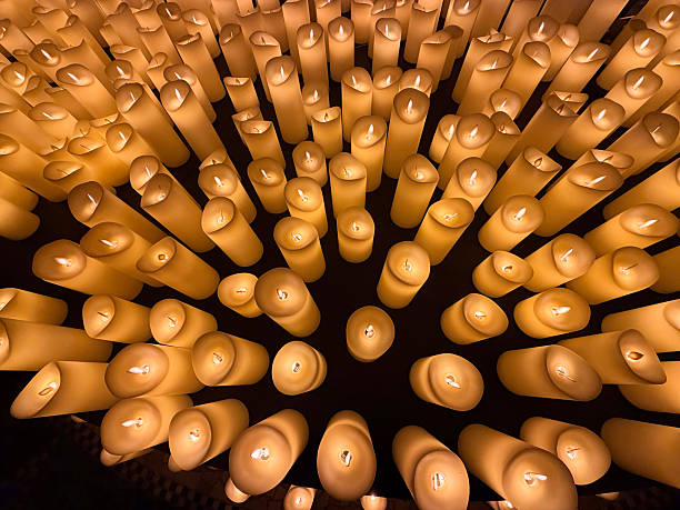 A large collection of flameless LED candles creates a warm, golden glow in a dark setting. The candles vary slightly in shape and height, forming a textured and atmospheric display. The soft, flickering light evokes feelings of peace, remembrance, and serenity, ideal for concepts related to spirituality, memorials, relaxation, and tranquil ambiance.