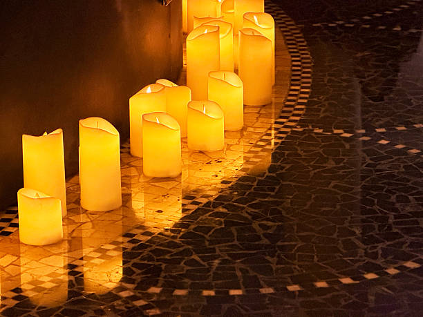 A large collection of flameless LED candles creates a warm, golden glow in a dark setting. The candles vary slightly in shape and height, forming a textured and atmospheric display. The soft, flickering light evokes feelings of peace, remembrance, and serenity, ideal for concepts related to spirituality, memorials, relaxation, and tranquil ambiance.