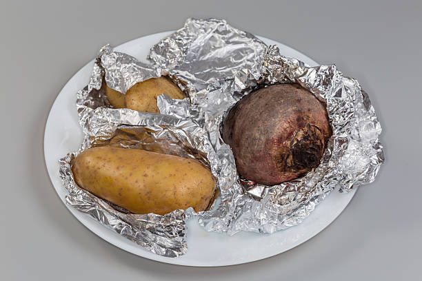 Homemade baked potatoes in an oven, served on a table at home in a rustic and vintage metal deep pan. Aerial view angle.