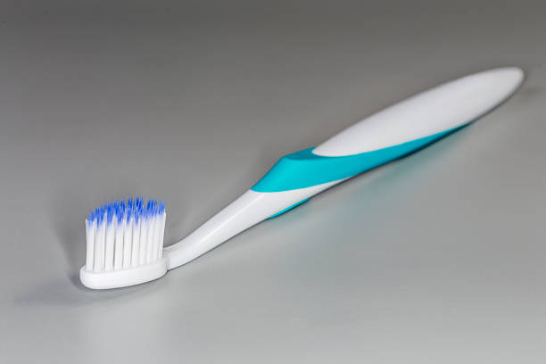 Modern traditional toothbrush with soft tops of bristles and ergonomic handle, close-up in selective focus on a gray background
