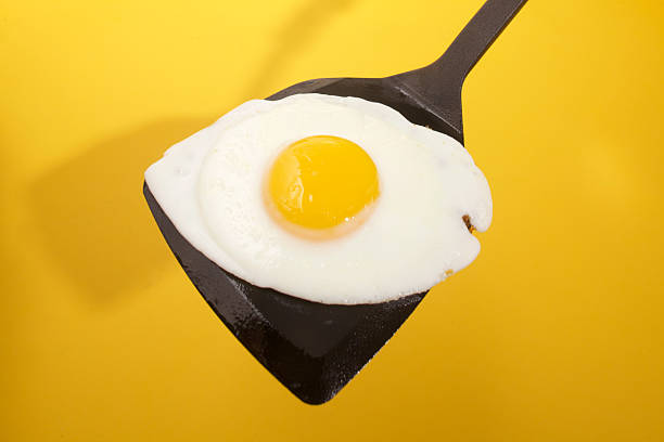 istock one fried egg on black spatula shot against yellow background 2251014382