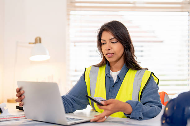 istock Female land surveyor reviews plans while using smartphone and laptop during office hours at project site 2251017280