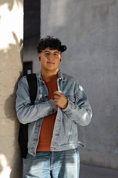 istock Young male student standing outdoors on university campus, wearing denim jacket and backpack, feeling confident and ready for education, learning, and future career 2251018197