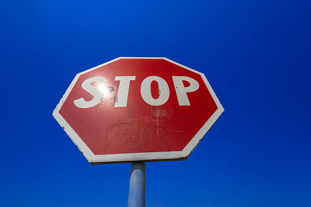 istock Stop Sign Against Bright Blue Sky: Red Octagonal Traffic Sign With Stickers and Weathered Surface 2251018917