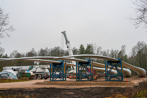 Large wind turbine blades rest on steel supports at forest construction site, with a crane and equipment ready for renewable energy installation work