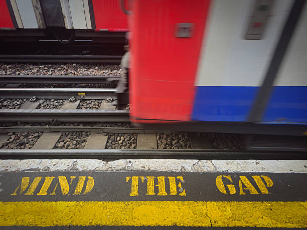 Yellow mind the gap text on a london subway platform with approaching train. Metro station warning sign