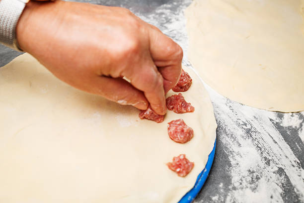 A hand places small portions of raw meat filling onto rolled dough while preparing homemade dumplings. Close-up of traditional cooking and food preparation