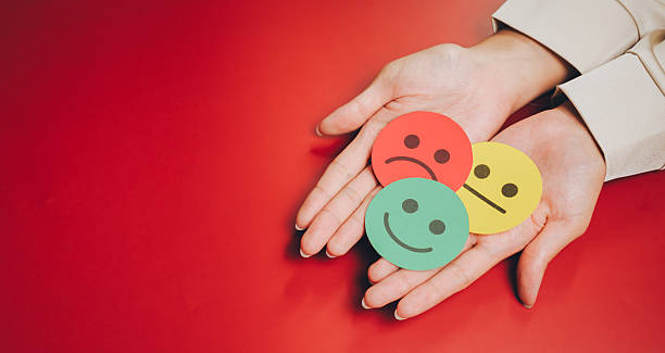 istock Feedback concept. Hands holding colorful paper cutouts of smiley faces representing different emotions on red background, symbolizing mood and feelings 2251035737