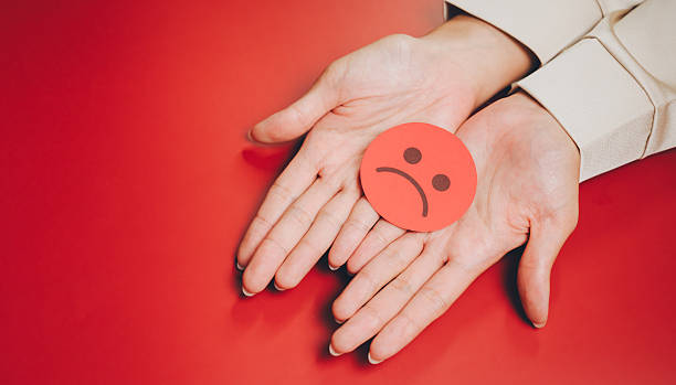 istock Feedback concept. Sad face icon hands red background emotion negative feeling human palms paper cutout isolated close up expression 2251035742