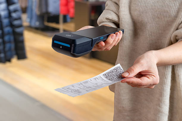istock Hand offering printed receipt with QR code next to POS terminal inside clothing store, showing modern payment and checkout workflow 2251037771
