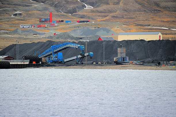 Longyearbyen, Spitsbergen, Svalbard, Norway: end of an era - coal loading terminal and conveyor belt infrastructure at the harbor. Large stockpiles of black coal are visible near the blue loading equipment on the shores of Adventfjorden. Historically, coal mining was the economic foundation of the archipelago, facilitated by the 1920 Svalbard Treaty, which grants signatory nations equal commercial rights to natural resources. However, the industry is in steep decline as Norway phases out fossil fuel extraction in the High Arctic. The state-owned mining company, Store Norske Spitsbergen Kulkompani, closed its final operating mine, Mine 7 (Gruve 7), in 2025, marking a definitive shift from an industrial mining settlement to a modern center for research and tourism.