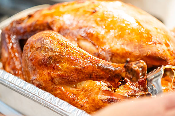 This is a photograph of a Thanksgiving turkey baked in an aluminum pan with the focus on the drumstick.
