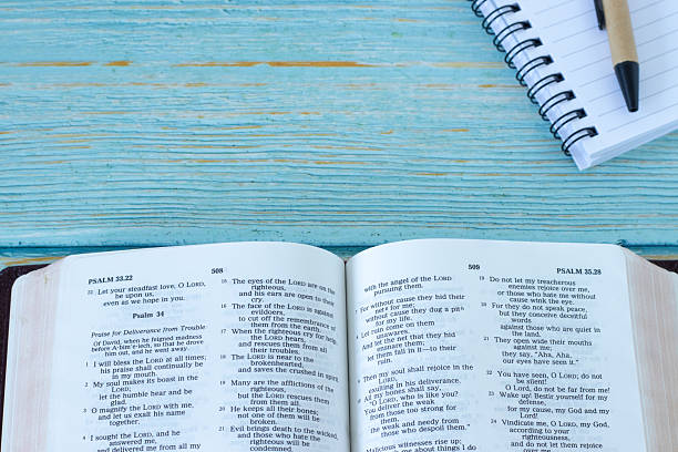 istock Open holy bible book with notebook on wooden table 2251052322