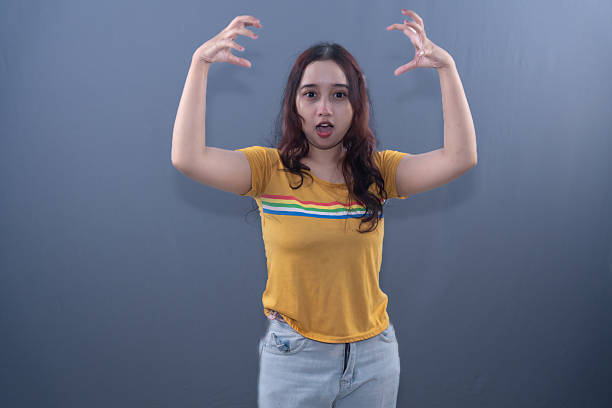 A woman in a yellow shirt makes a 'monster claw' pose with a surprised expression