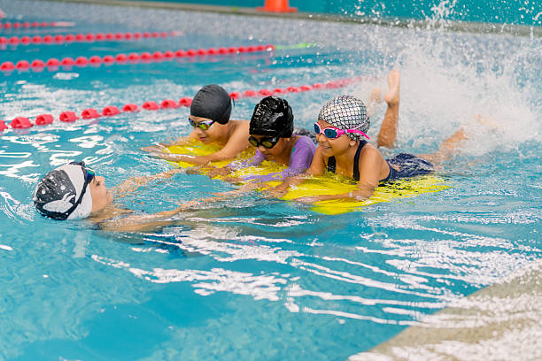istock Children learning to swim in pool with instructor using kickboards 2251058431