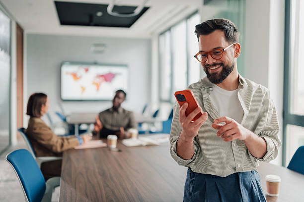 istock Smiling man using smartphone in modern office meeting 2251060350