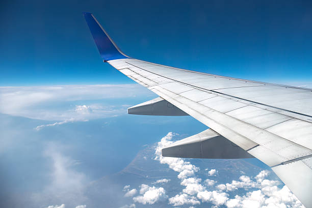 istock Airplane wing flying over white clouds and blue sky 2251062377