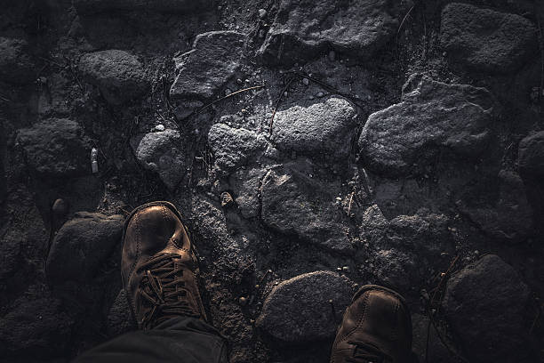 Hiker is standing on a rocky trail, looking down at his hiking boots, taking a break from hiking