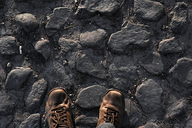 Traveler is standing on a cobblestone road with brown hiking boots, taking a break from exploring