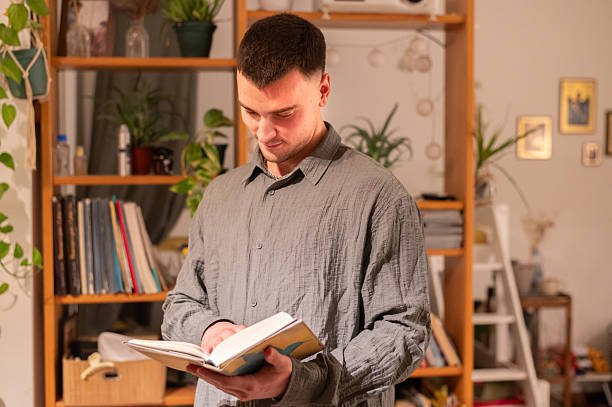 istock Young smiling man reading a book at home 2251065595