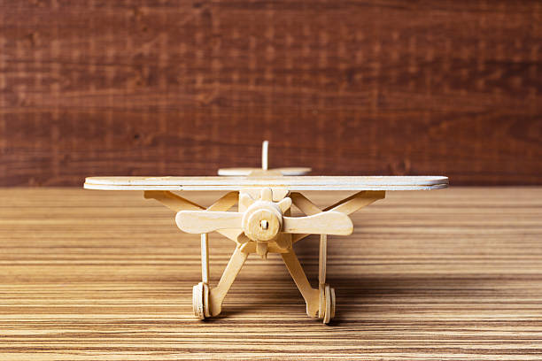 A wooden model airplane with detailed features sits on a wooden table in a craft studio.