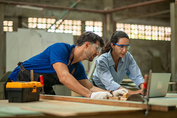 istock Carpenter with supervisor works on measuring and adjusting wooden piece on  workbench while checks project details on laptop craftsmanship with digital technology planning 2251070054