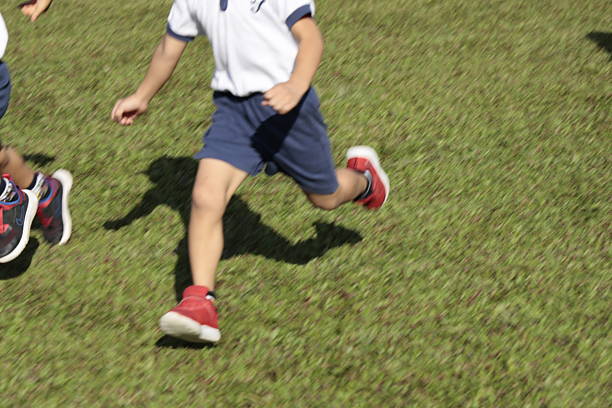 Children in athletic wear run across a grassy field, captured mid-motion with focus on legs and shoes.