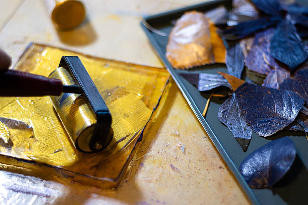 istock Brayer spreading golden paint on gelli plate beside gathered lea 2251080145