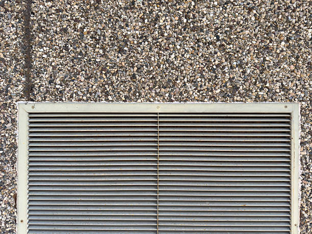Metal HVAC ventilation grille on a weathered pebble dash wall, showing a textured exterior
