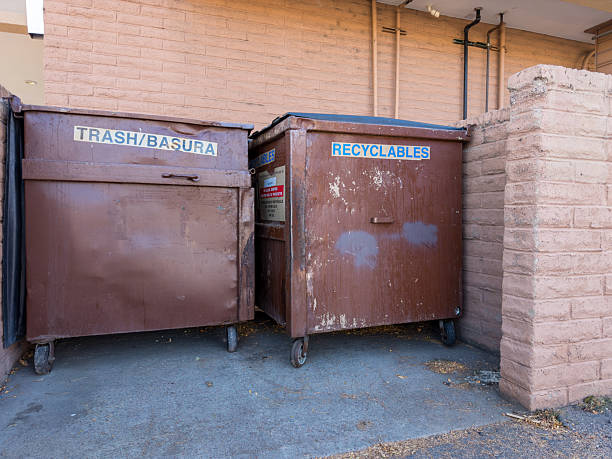Brown dumpsters for trash and recycling standing next to a brick wall
