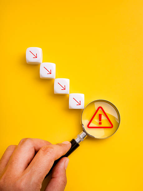 White cubes with downward red arrows and warning icon under magnifying glass symbolize business crisis, market crash, financial risk, rapid decline, alert signal, and critical economic downturn.