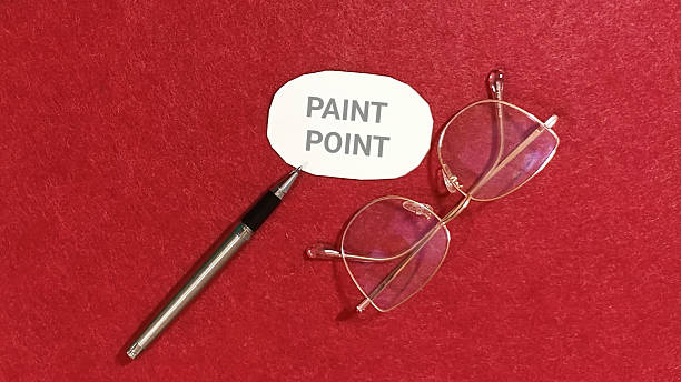 Paint point concept represented by a small white card featuring the words beside a silver pen and a pair of reading glasses resting on a textured vibrant red surface suggesting the need for precise f