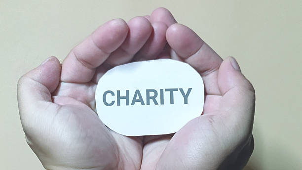 istock Cupped hands tenderly cradle a small white oval card featuring the bold word charity symbolizing the profound human connection to giving. 2251092541
