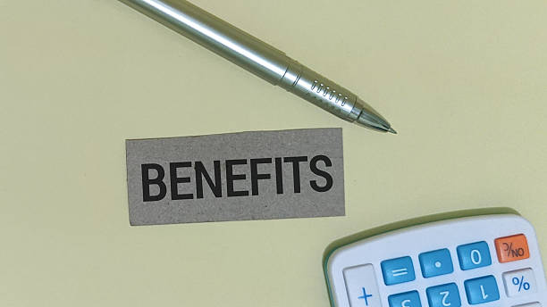 istock Employee benefits concept is visually represented by a small cardboard label featuring the word benefits resting on a light yellow surface next to a silver pen. 2251095548