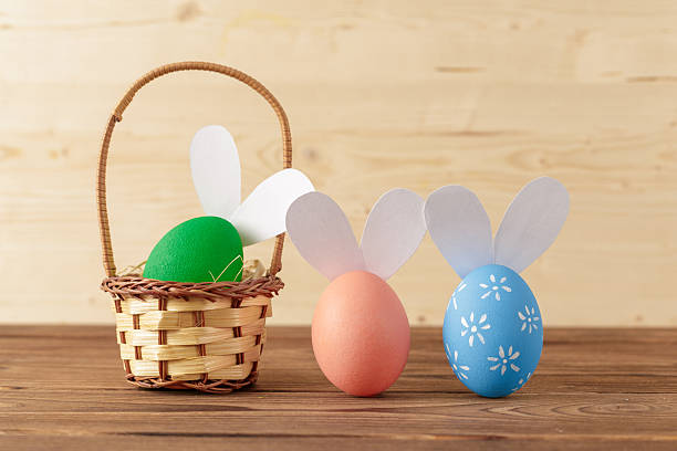 istock Colorful Easter eggs with bunny ears in a small basket on a wooden table 2251101870