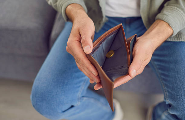 istock Man who is experiencing a financial crisis opens his wallet with a single coin inside 2251103118