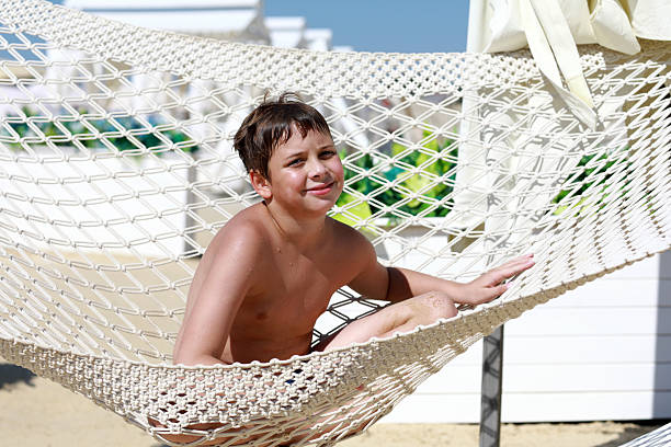 Happy boy child relaxing in a hammock on the beach. Summer sun vacation concept. Calm relaxing leisure time for a kid.