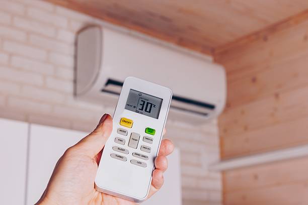 istock Controlling Indoor Climate: A Hand Holding a Remote for an Air Conditioning Unit Set at 30 Degrees Celsius in a Cozy Room 2251107085