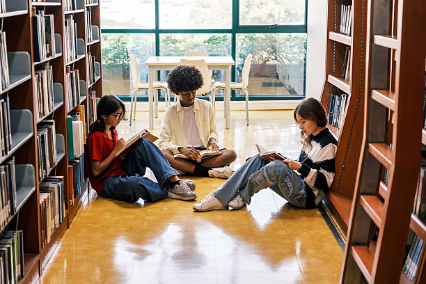 istock Three diverse studentsIndian, African, and Asiansit together on the library floor between bookshelves, reading, discussing books in bright, academic environment filled with learning and imagination 2251126624